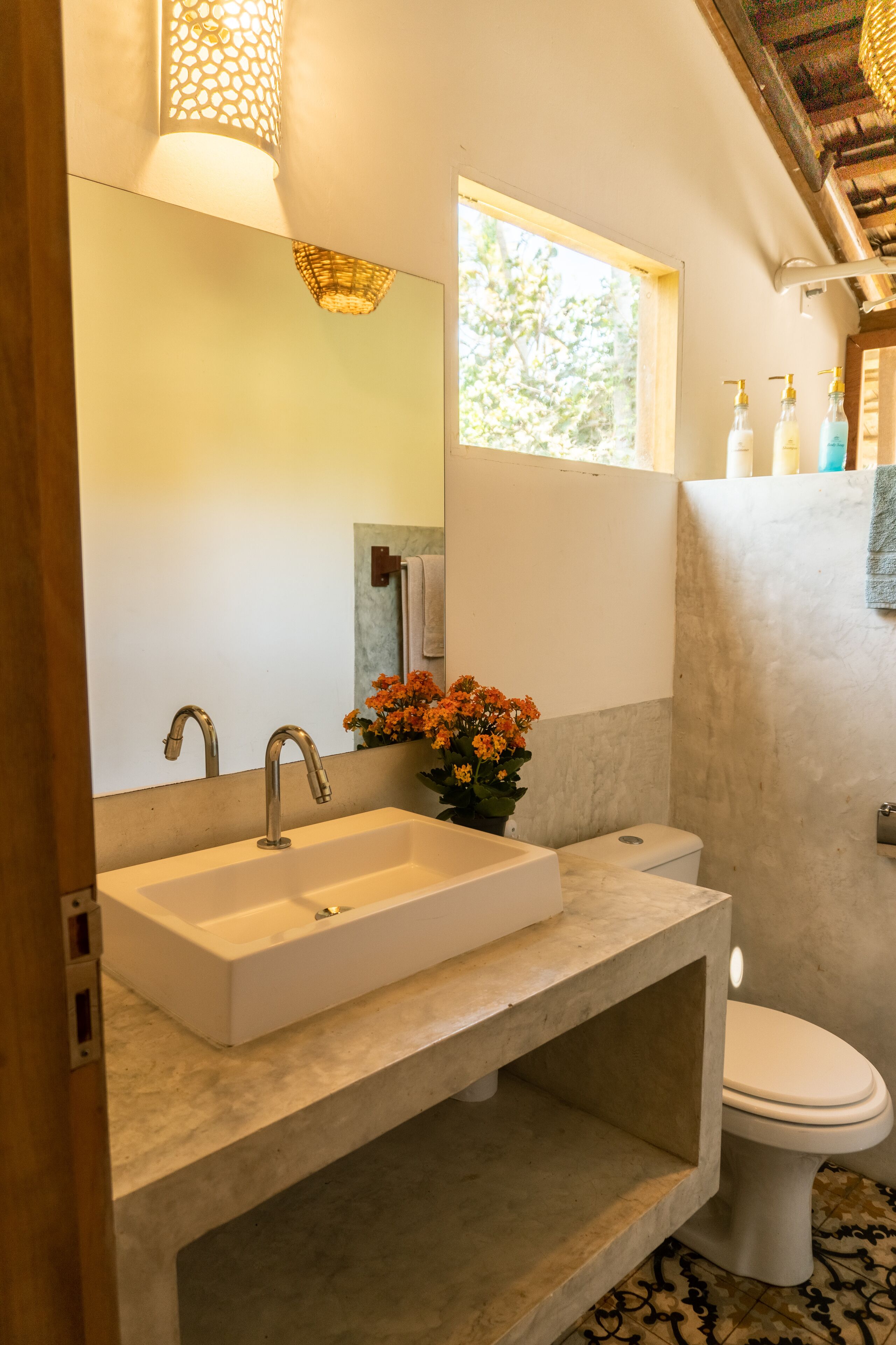 Une salle de bain avec un grand miroir, un lavabo, des toilettes et une fenêtre.