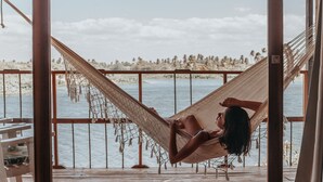 Un'amaca su un pontile di legno con vista su una spiaggia e palme.