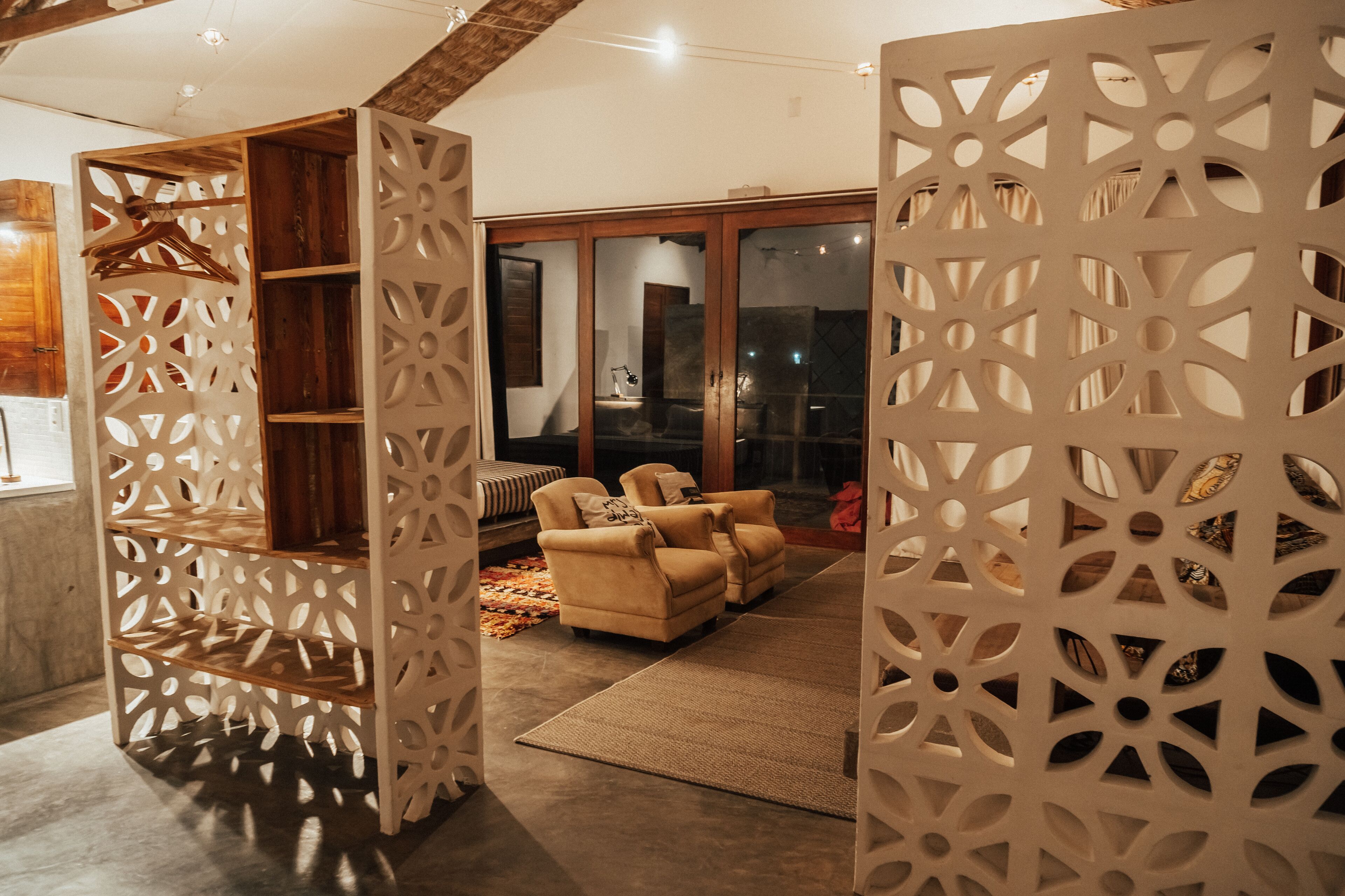 A modern living room with a sofa set, a wooden bookshelf, and a decorative screen with geometric patterns.