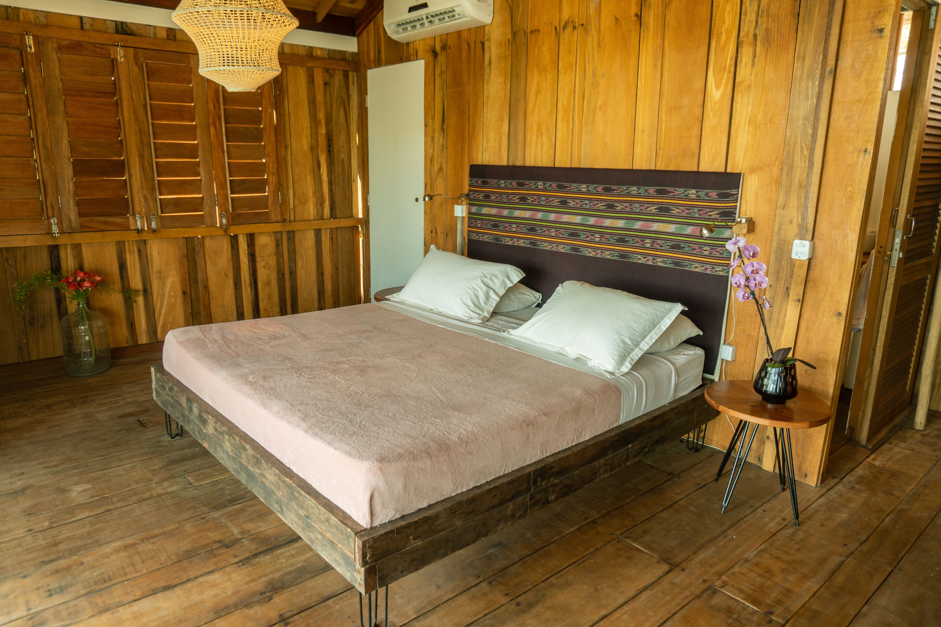 A wooden room with a bed, a small table, and a hanging light fixture.