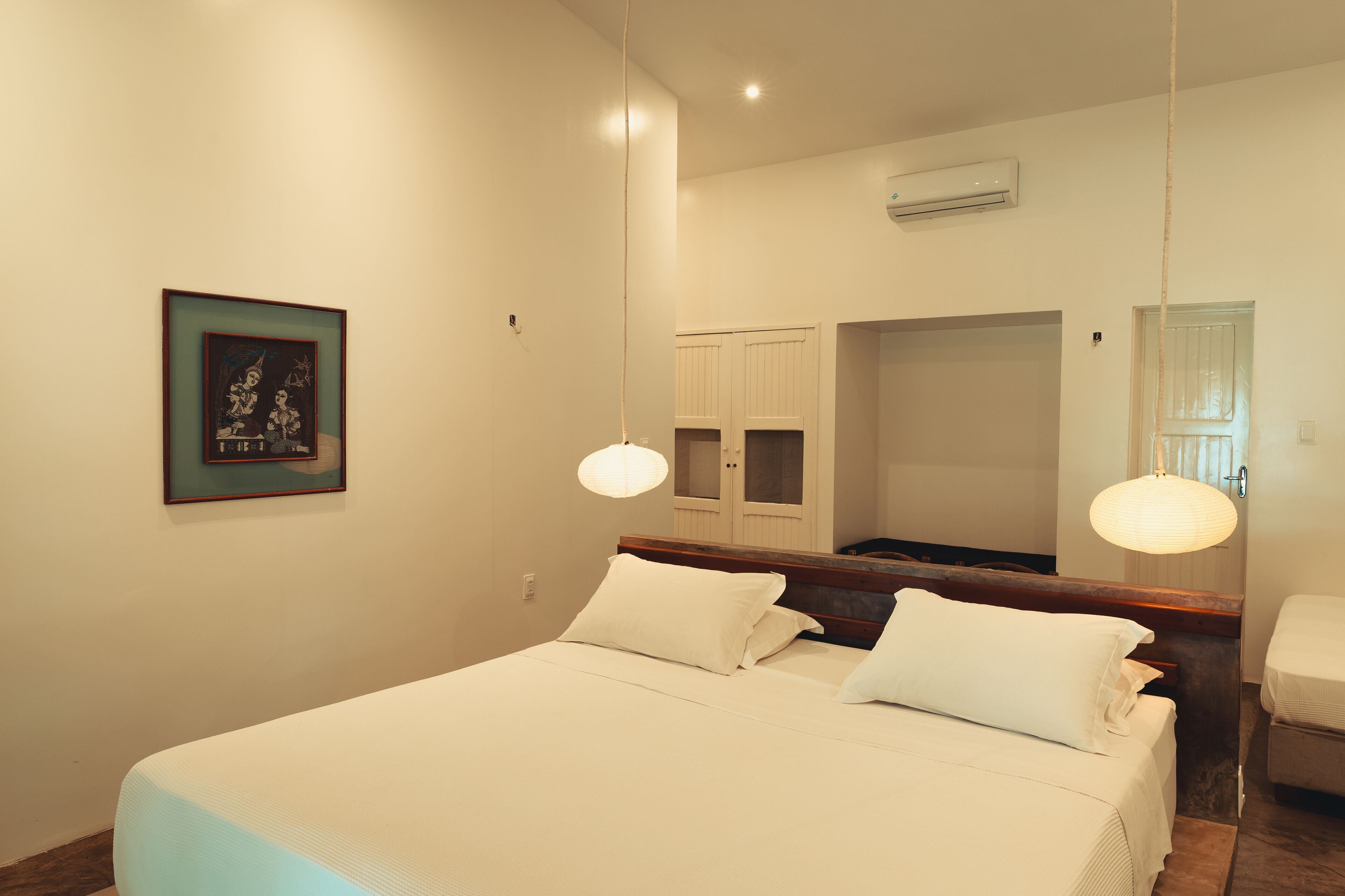 A bedroom with a large bed, a wooden headboard, a bedside table, a hanging light, a framed picture on the wall, and a wardrobe.