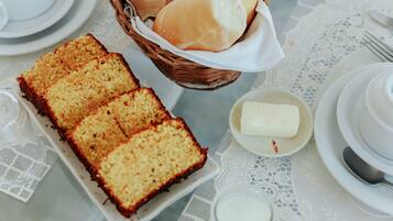 Una mesa adornada con un mantel de encaje blanco, un plato de pastel, una cesta de bollos y un tazón pequeño de mantequilla.