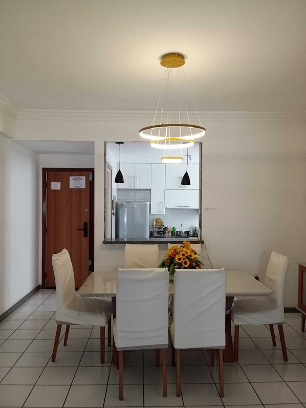 A dining area with a white table and chairs, a vase of sunflowers, and a kitchen visible through a large mirror.