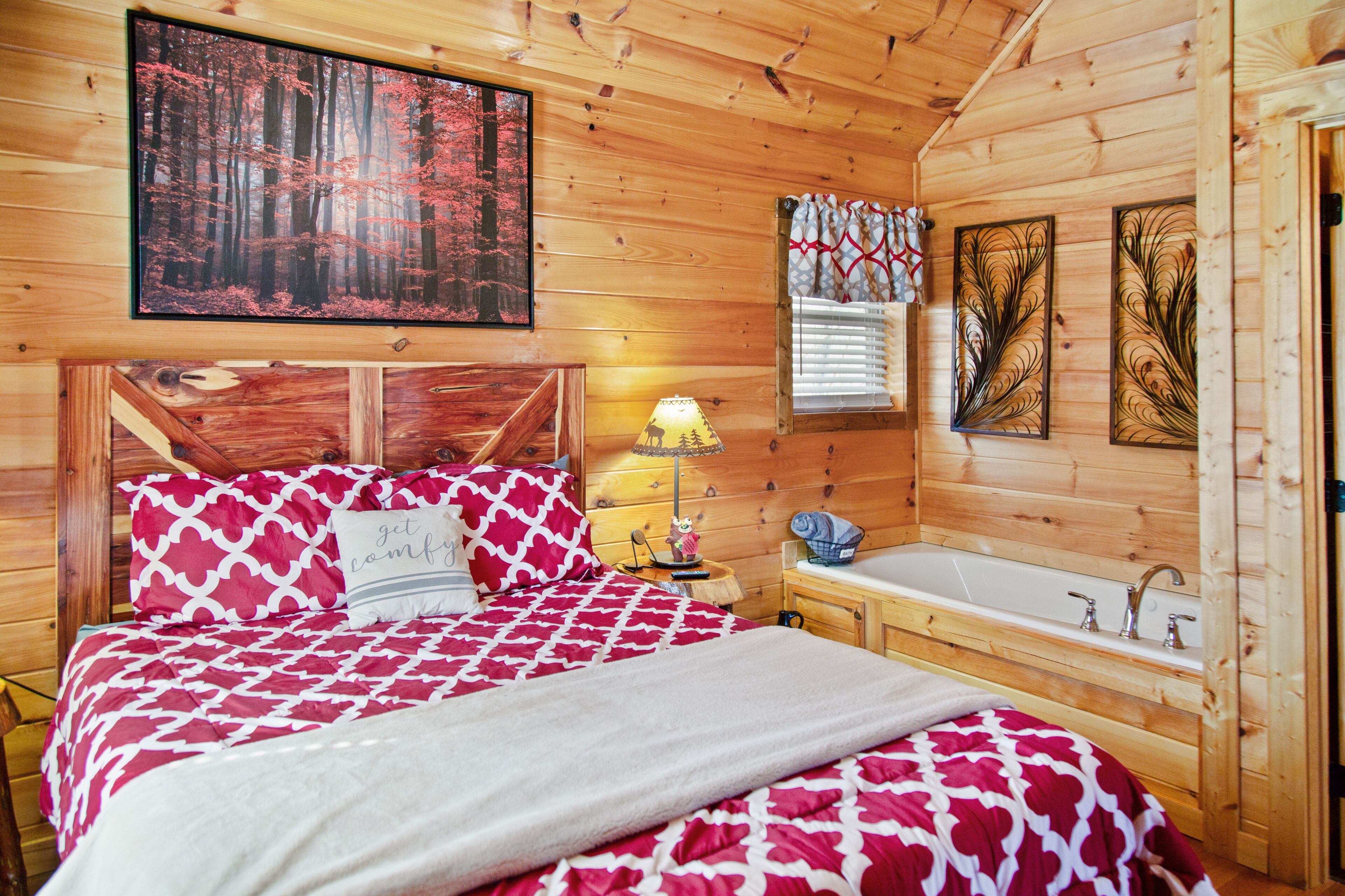A wooden cabin bedroom with a bed, a nightstand, a lamp, a window with blinds, and a wooden bathtub.