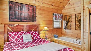 Quarto de cabana de madeira com cama, mesa de cabeceira, abajur, janela com persianas e banheira de madeira.