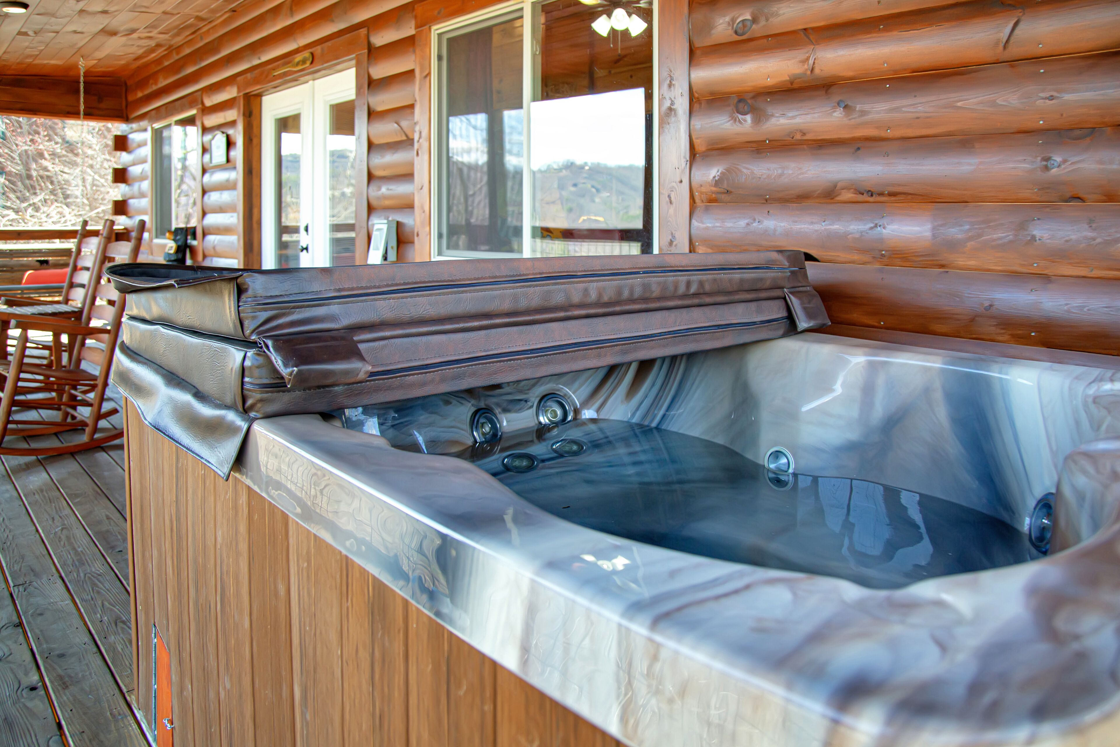 A wooden cabin with a hot tub and wooden deck chairs.
