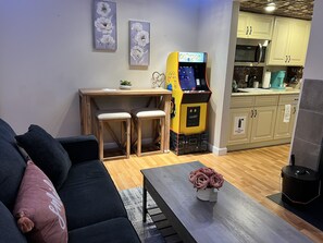 Cozy living space with a sofa, coffee table, and desk area featuring a Pac-Man arcade game.