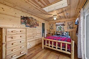 Une chambre dans une cabane en bois, avec un lit, une commode et des œuvres d’art accrochées aux murs.
