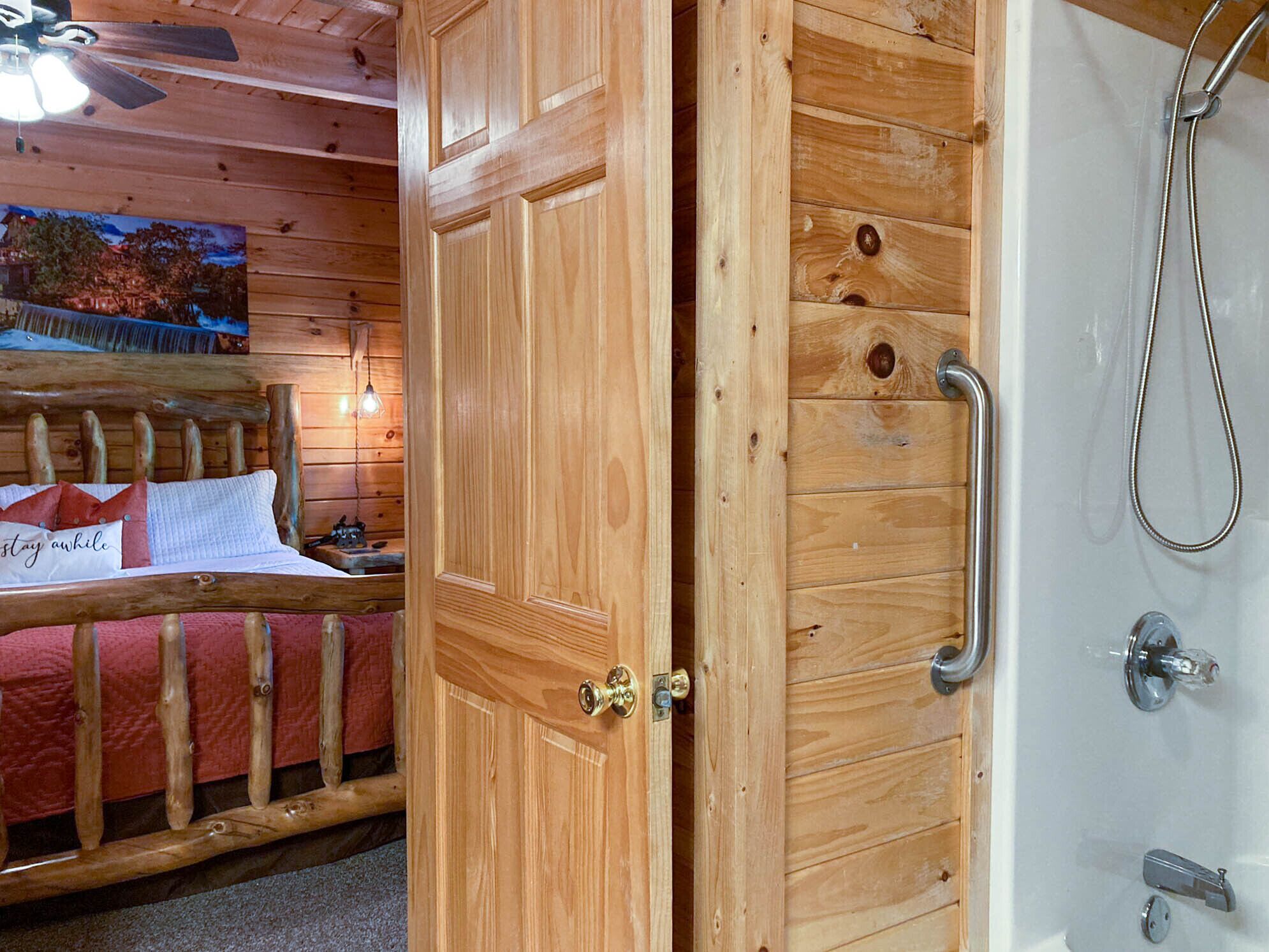 A wooden door leading to a room with a bed, a nightstand, and a shower area.