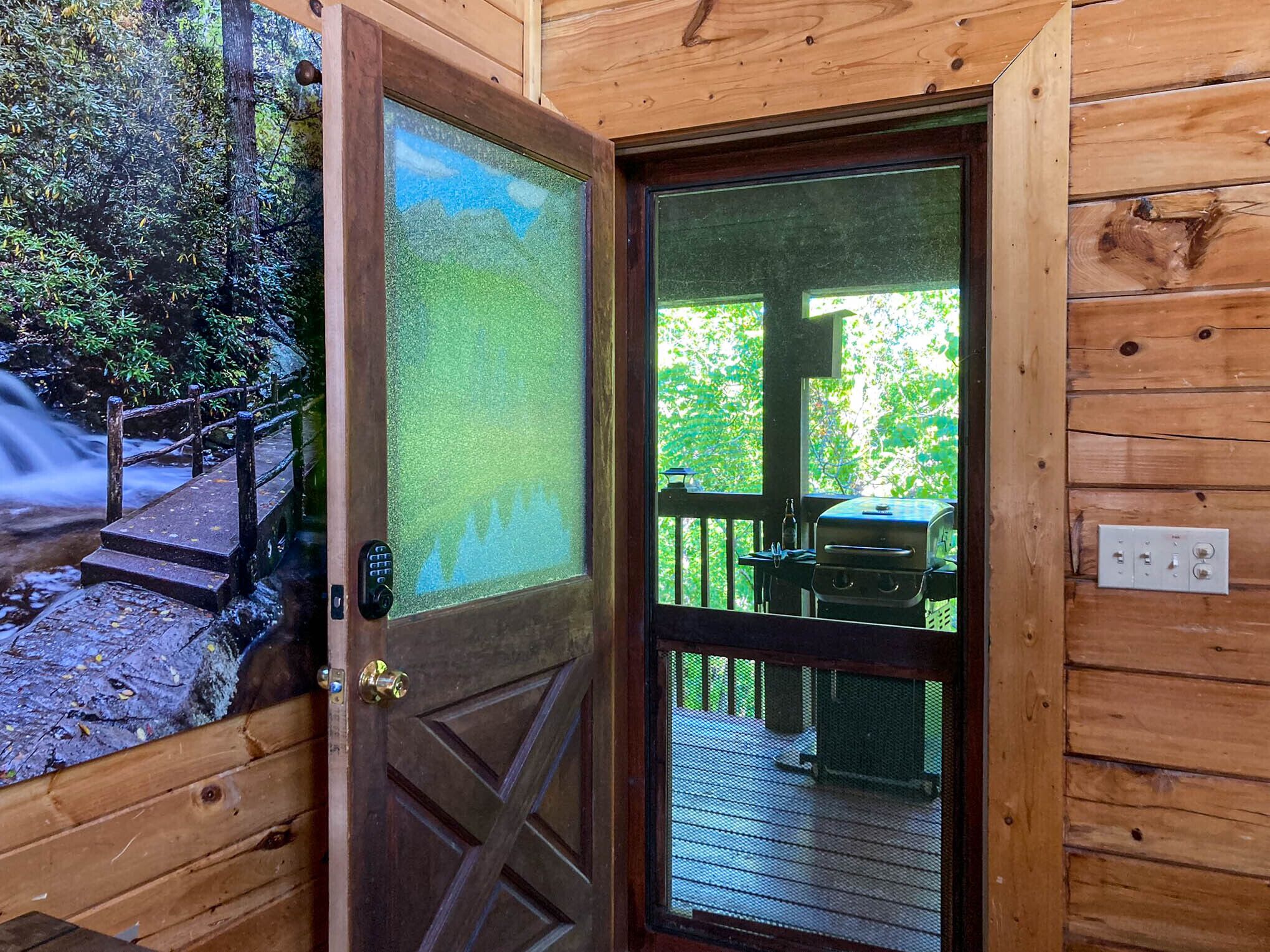 A wooden cabin entrance with a glass door, a wooden deck, and a grill outside.