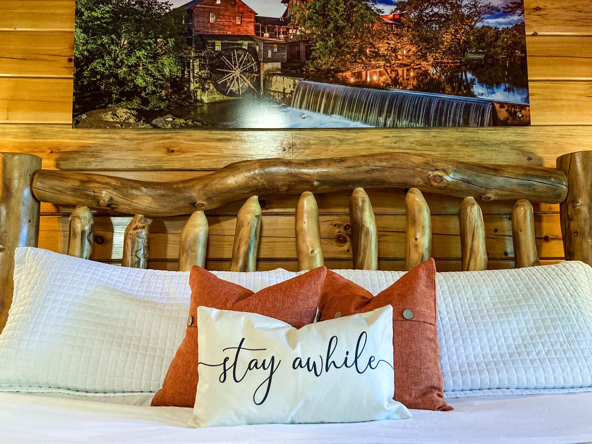 A wooden headboard with a rustic design, a bed with white bedding, and a pillow with the text "stay awhile".
