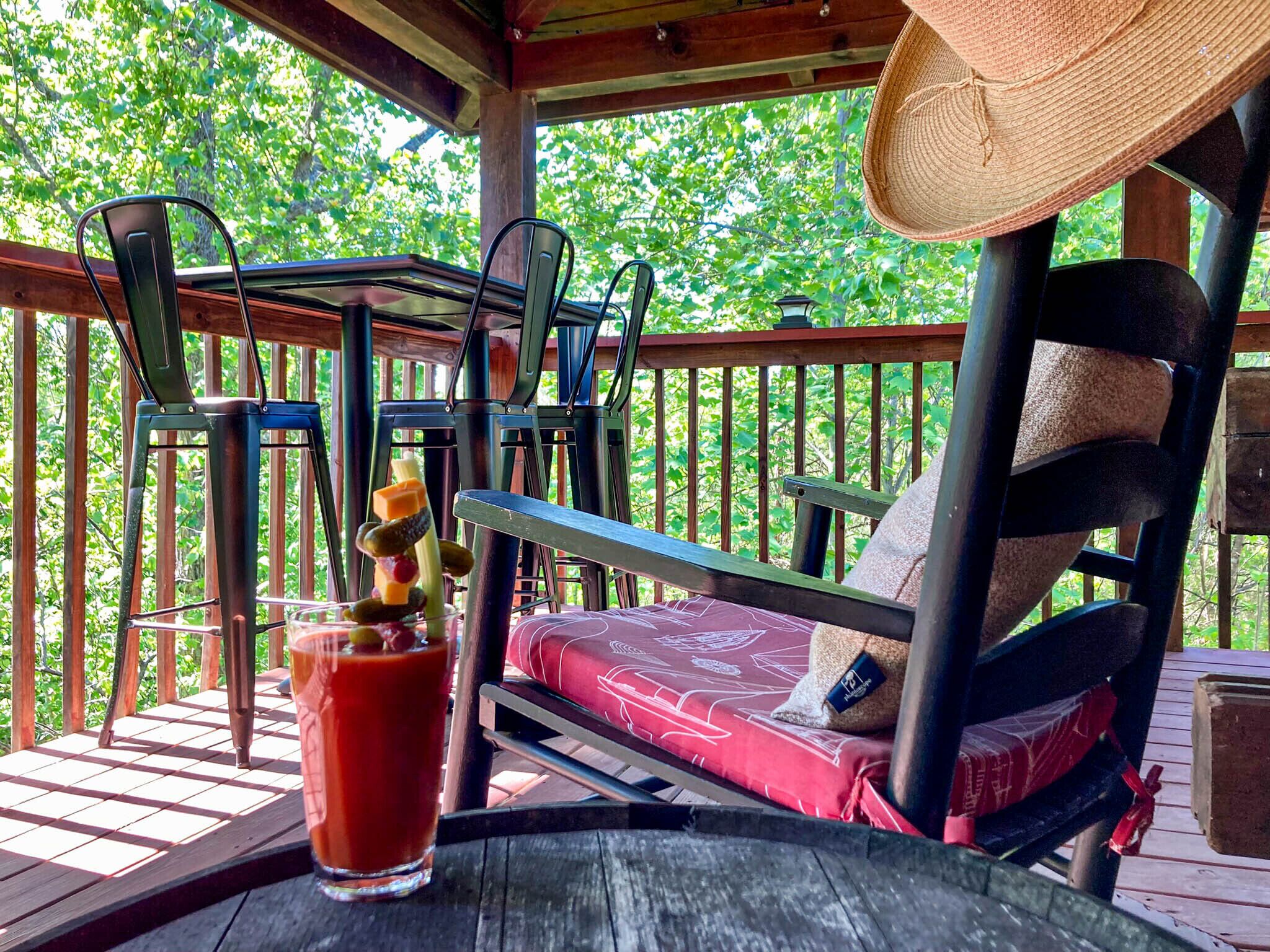 Una terraza de madera con un banco acolchado rojo, un vaso de bebida roja y un sombrero de paja.