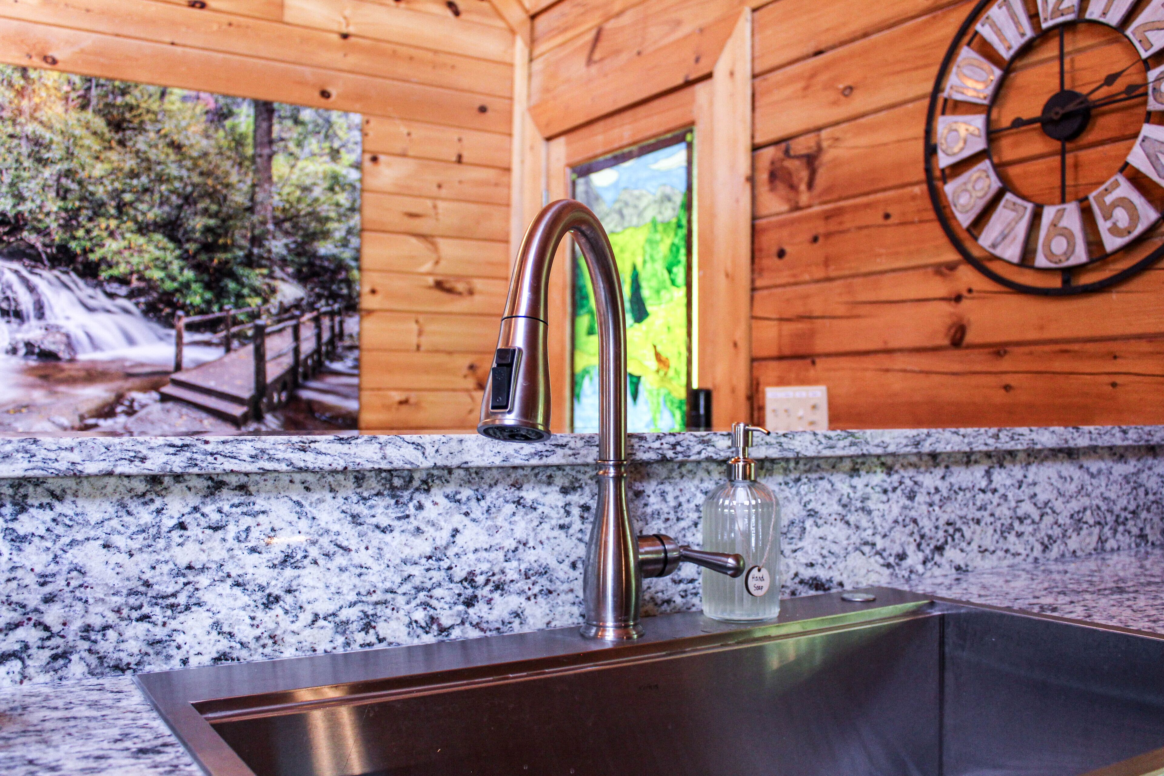 A kitchen with a stainless steel sink, granite countertop, wooden walls, and a wall clock.