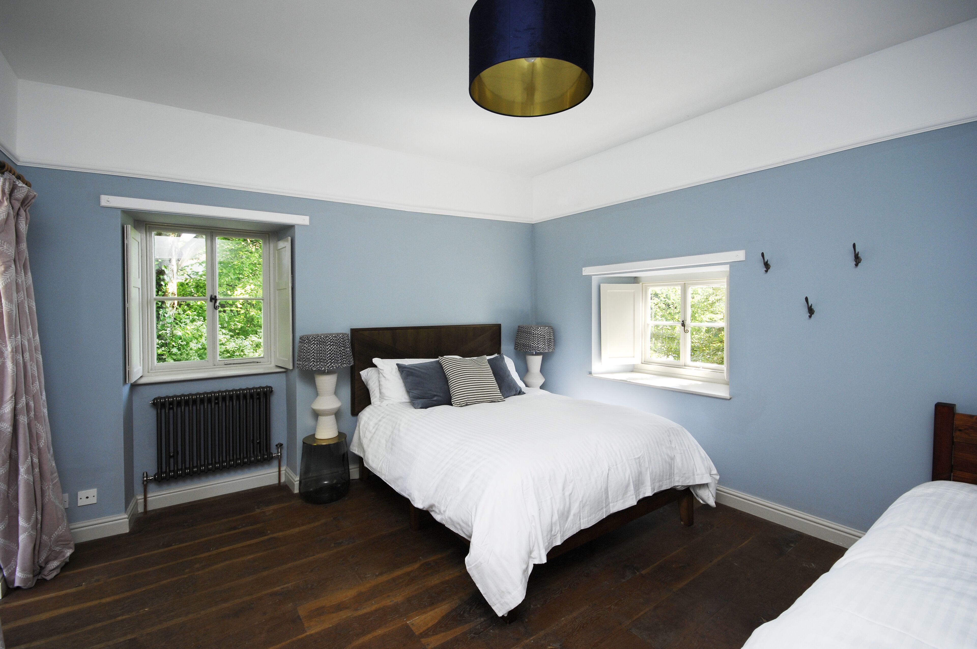 A bedroom with a bed, two bedside tables, a window, and a radiator.