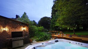 A backyard with a stone barbecue, a hot tub, and a dining area with outdoor furniture. - Beautiful 7 bedroom house hottub wifi (Shepton Mallet)