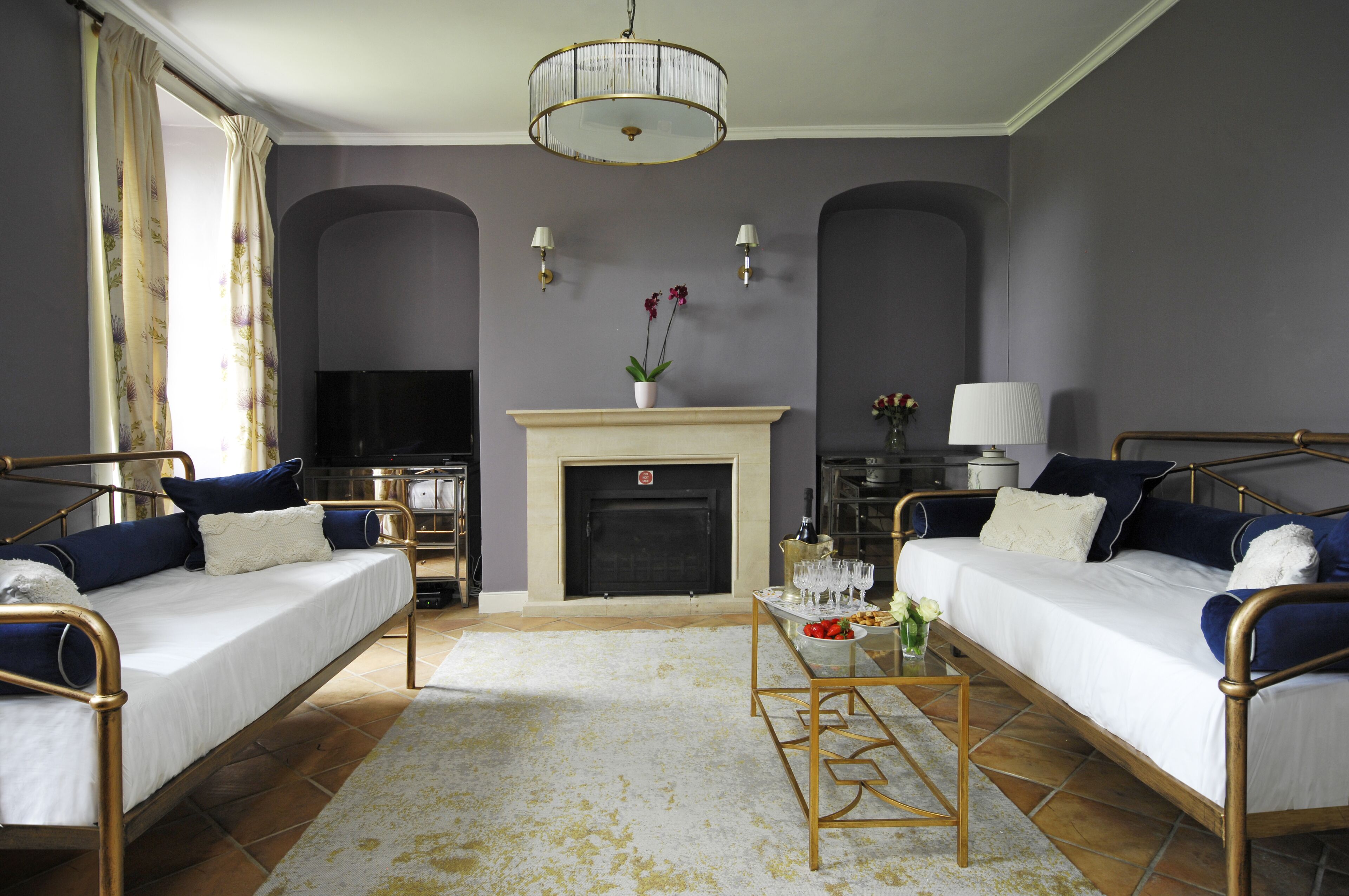 Ein Zimmer mit zwei Betten, einem Kamin, einem Fernseher und einem Esstisch mit einem Blumenstrauß.