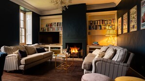 A cozy living room with a fireplace, striped sofas, a coffee table, and a bookshelf filled with books. - Beautiful 7 bedroom house hottub wifi (Shepton Mallet)