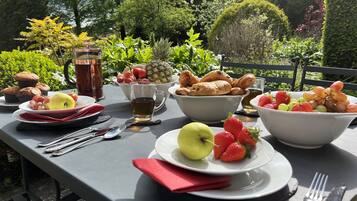 A table set with breakfast items including fruits, pastries, and beverages, surrounded by greenery.