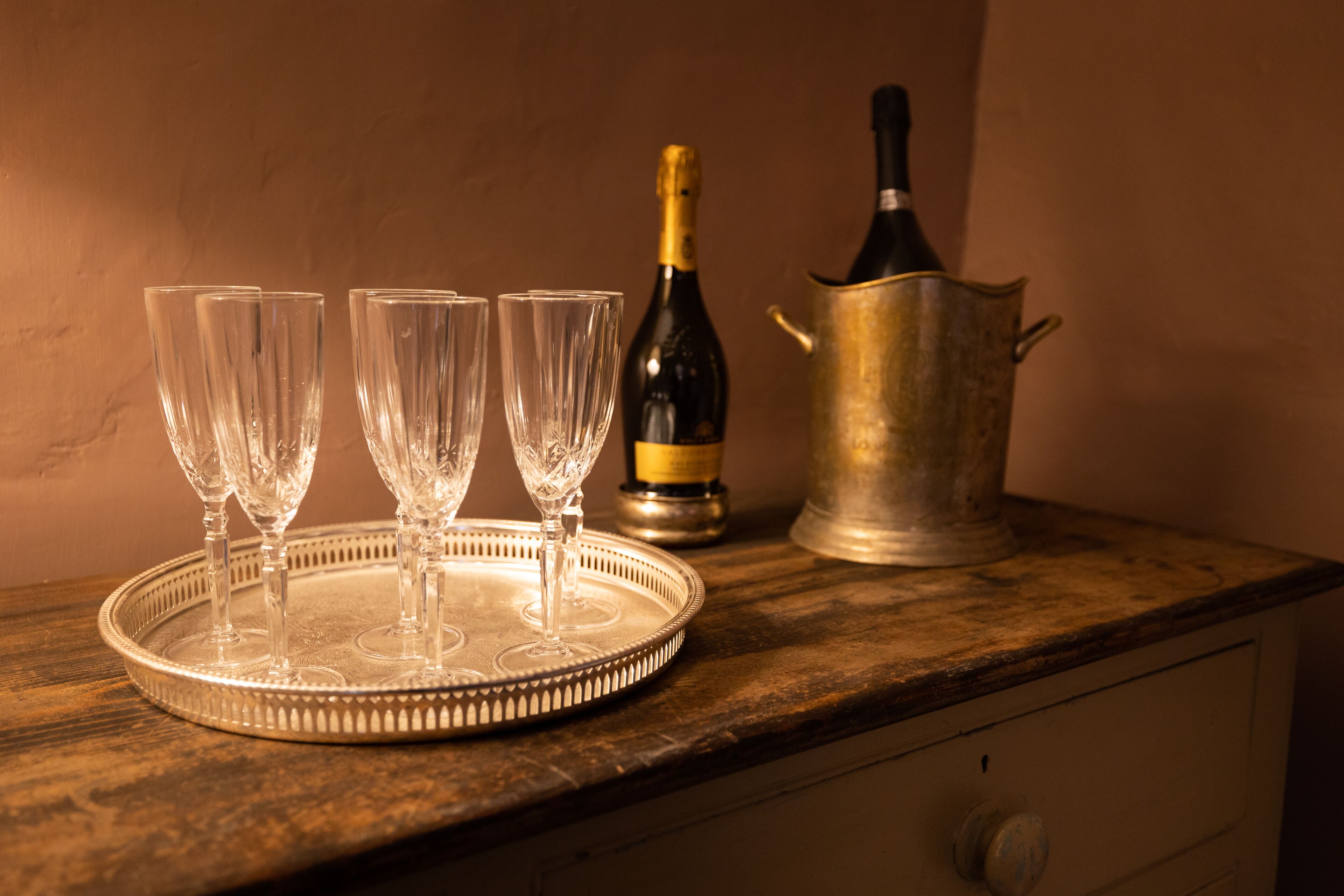 A tray with three clear glasses and a bottle of champagne on a wooden table.