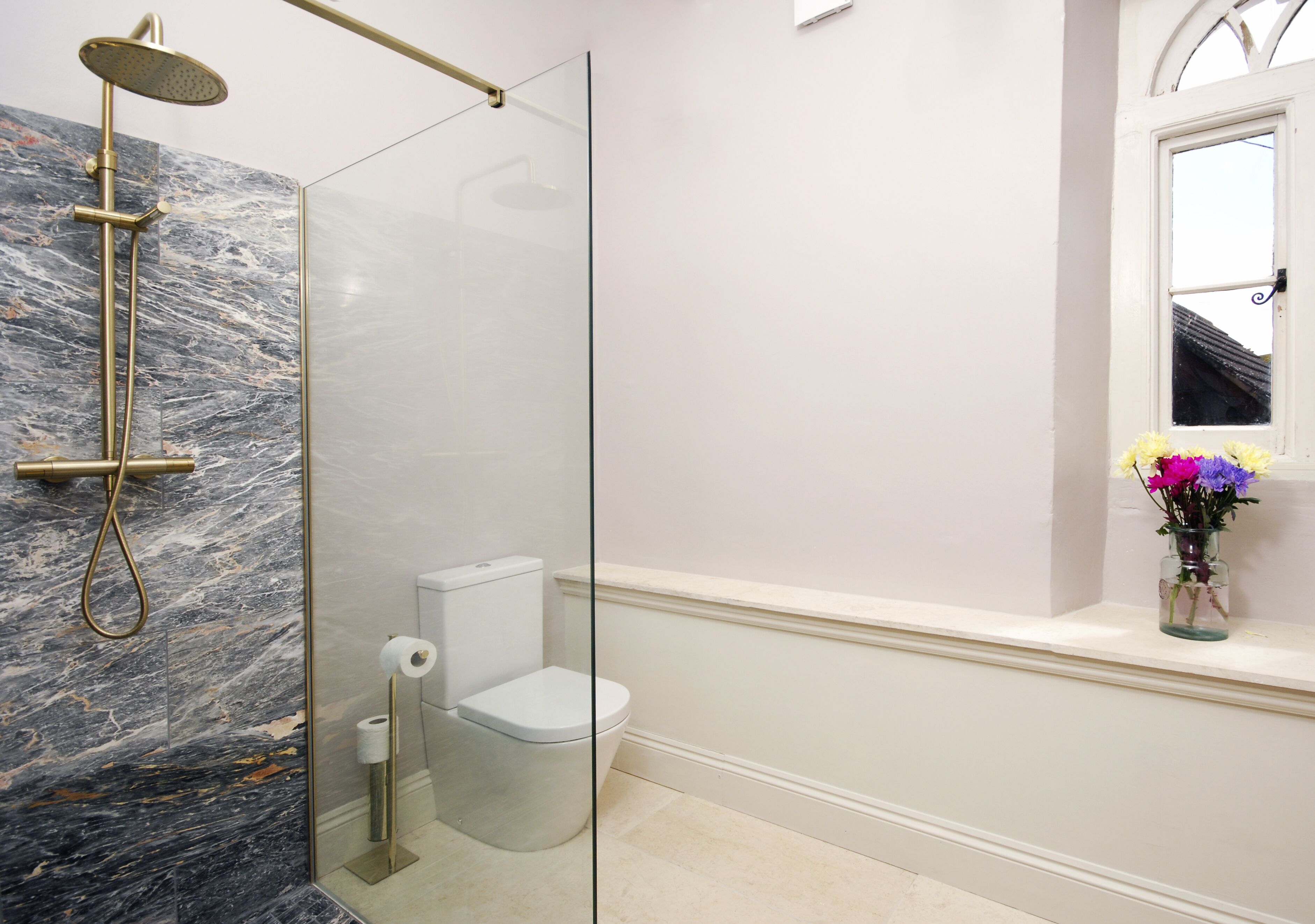 Un baño con ducha de vidrio, inodoro y ventana con un florero.