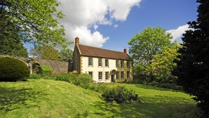 A traditional two-story house with a stone wall and a well-maintained lawn. - Beautiful 7 bedroom house hottub wifi (Shepton Mallet)