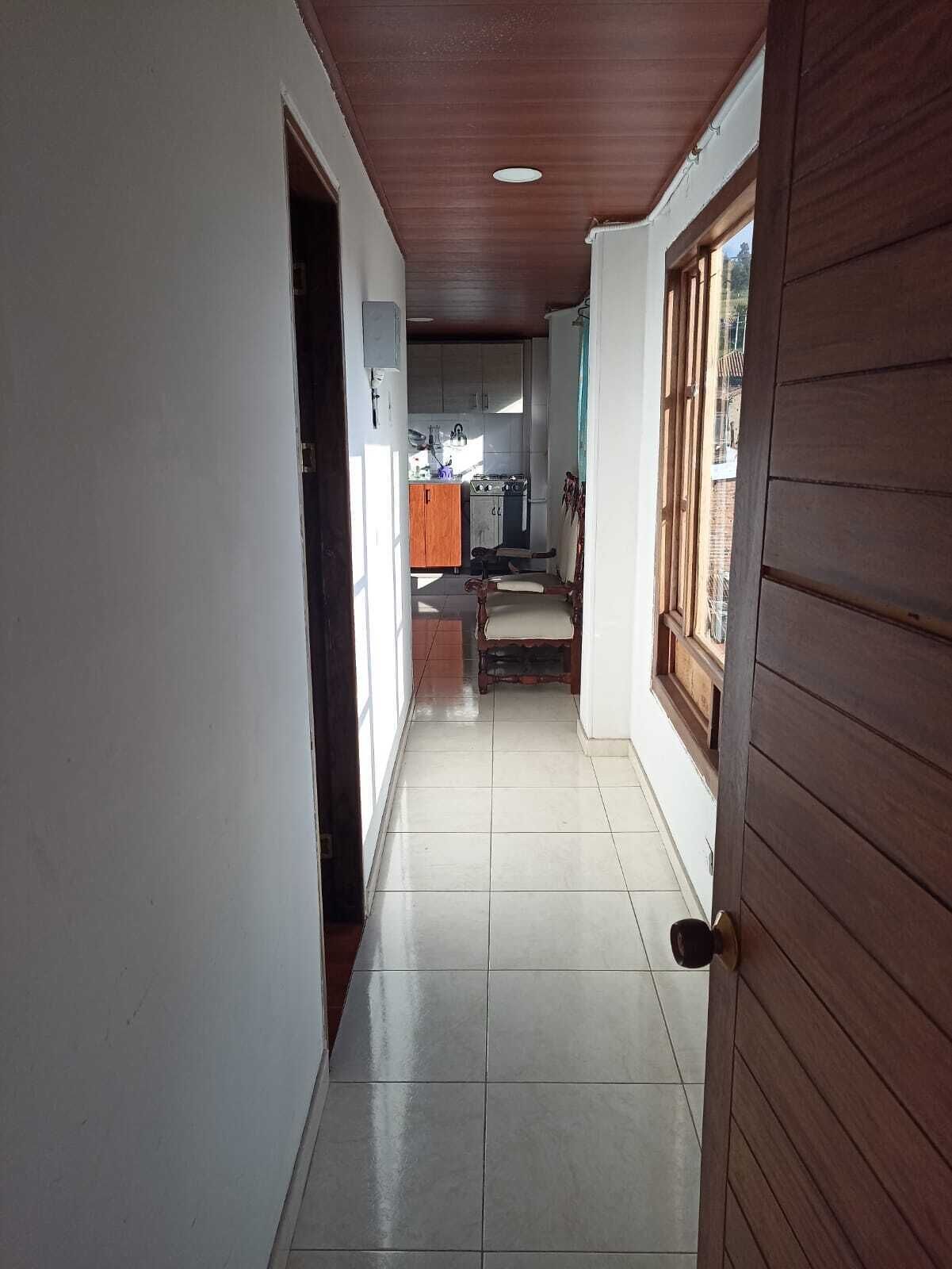 Un couloir avec une porte en bois sur la droite, qui donne sur un espace cuisine aménagé avec des placards et un fourneau.