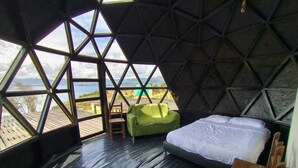 A room with a bed, a green chair, and a view of the outdoors through large windows. - Hotel Tota Eliseo Playa Blanca (Tota)
