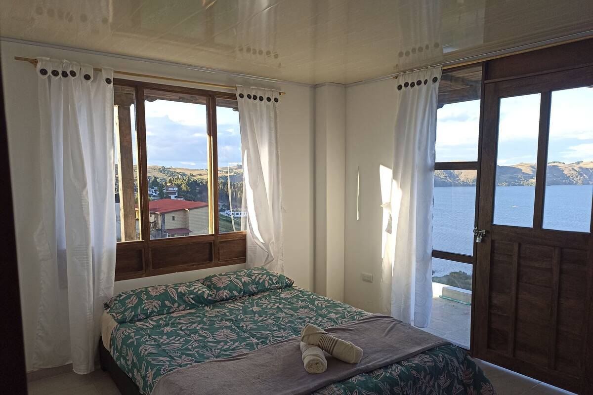 Un dormitorio con cama, vistas a un lago y ventana con cortinas.