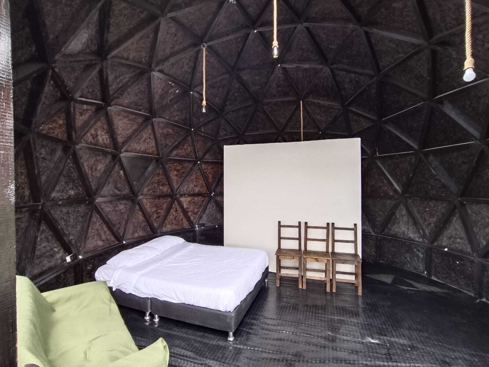 A room with a geometric-patterned wall, a bed with a white mattress, a wooden ladder, and a light bulb hanging from the ceiling.