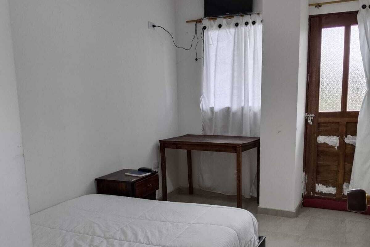 Un dormitorio con una cama individual, una mesita y una puerta que da a otra habitación.
