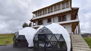 A modern building with two geodesic dome structures in front, a wooden deck, and a staircase leading to the entrance. - Hotel Tota Eliseo Playa Blanca (Tota)