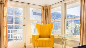 Une pièce lumineuse avec un fauteuil jaune, de grandes fenêtres et une lampe en laiton.
