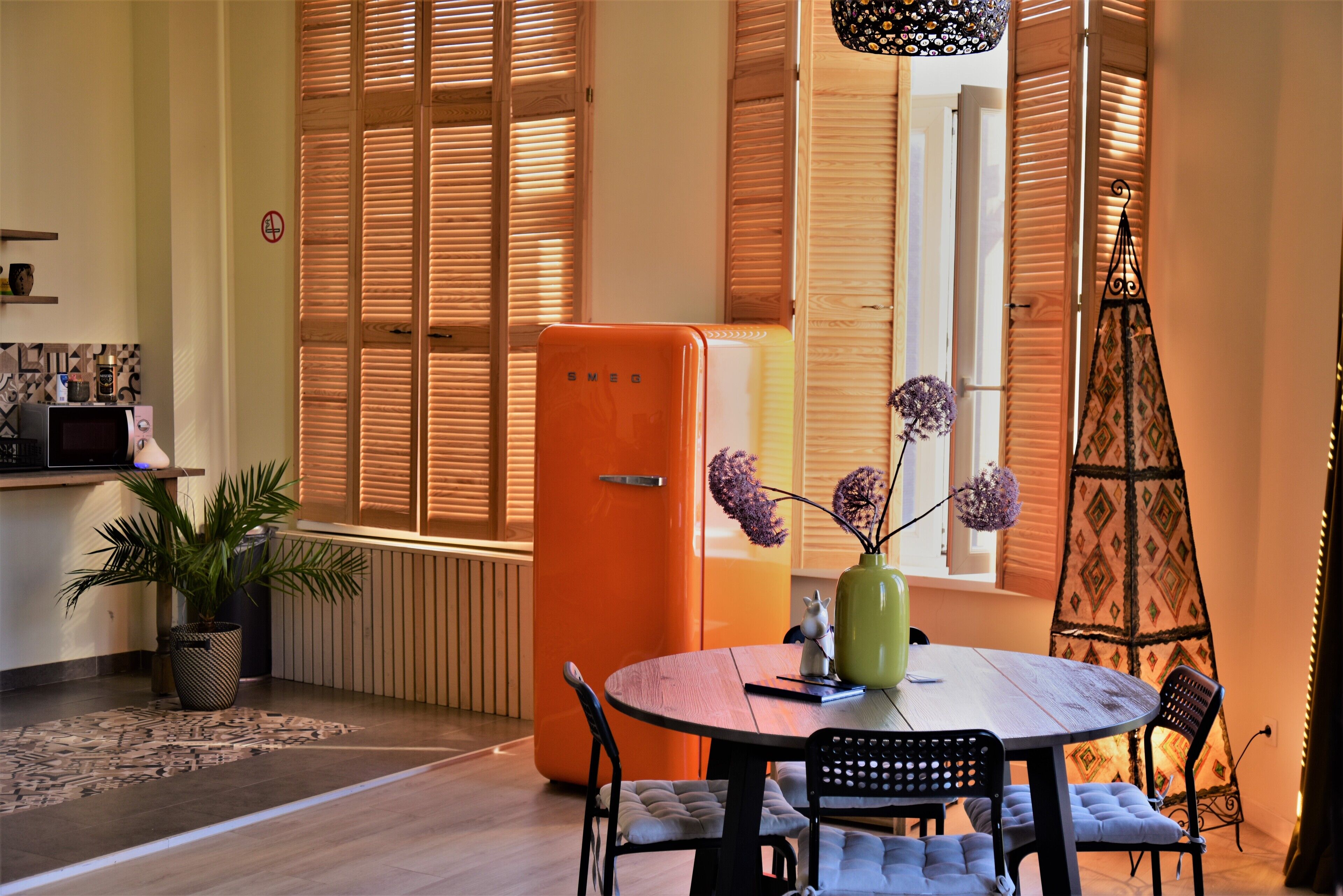 A compact living space with a dining area, a kitchen with a microwave, and a window with wooden shutters.