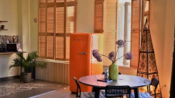 A compact living space with a dining area, a kitchen with a microwave, and a window with wooden shutters.