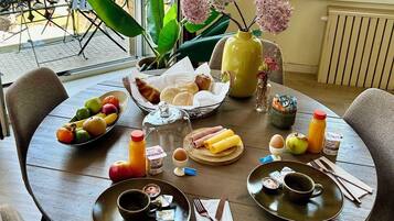 A dining table set with breakfast items, including fruits, bread, and beverages, in a room with a view of the outdoors.