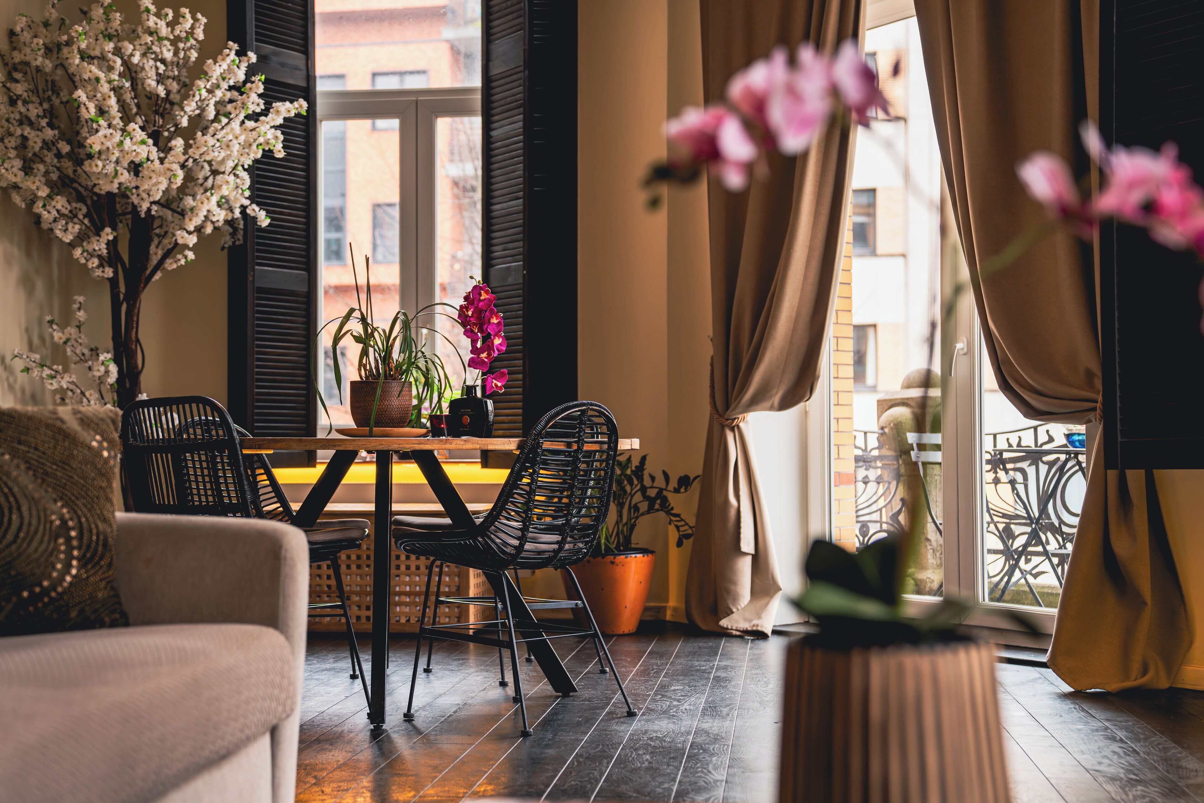 Un cuarto acogedor con una mesa de comedor, sillas y un sofá. Tiene una ventana con cortinas, una planta en maceta y vistas al exterior.