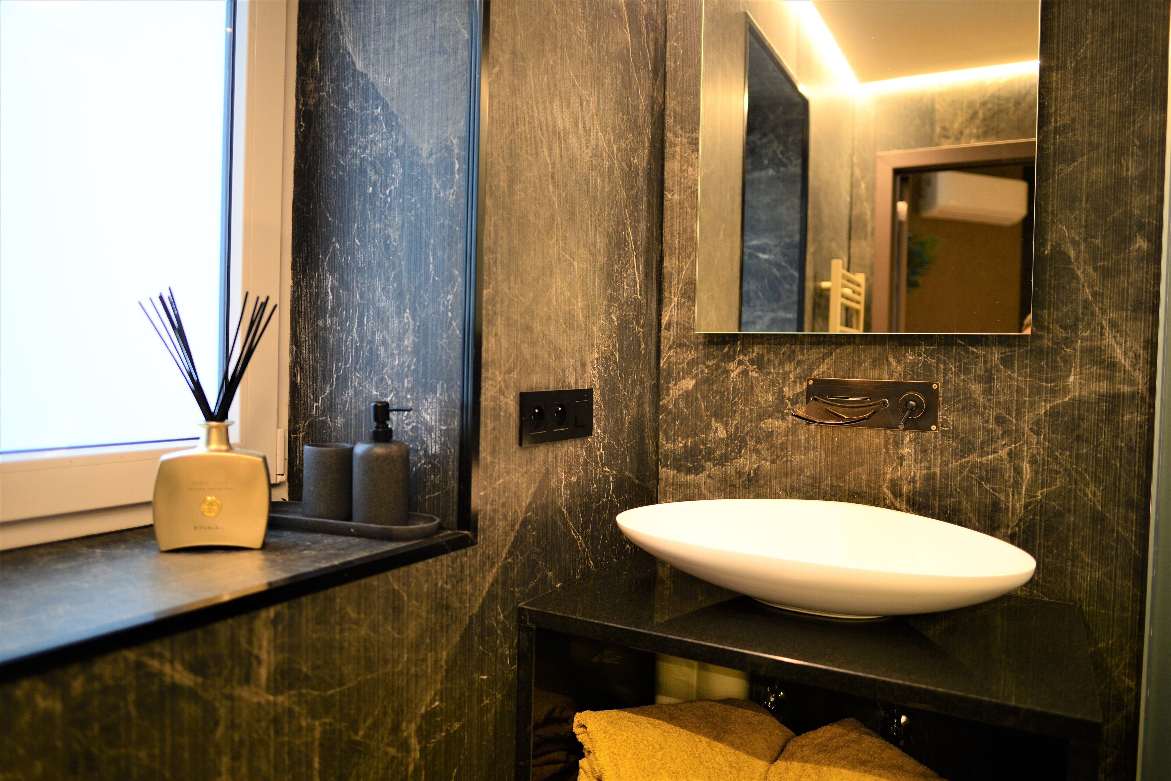 A bathroom with a large mirror, a white sink, and a window.
