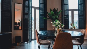 Una mesa redonda para comer con cuatro sillas, un florero con flores y vistas al exterior a través de contraventanas negras abiertas.
