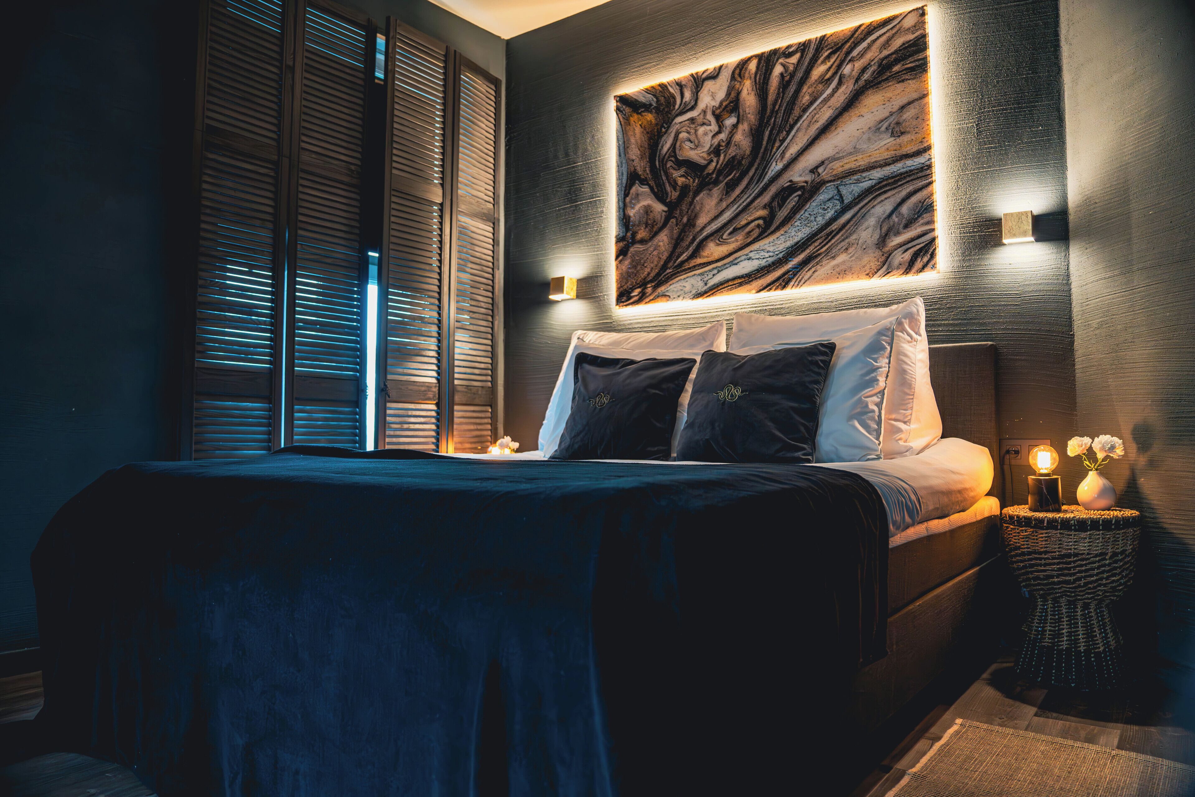 A modern bedroom with a large bed, a marble wall art piece, and a nightstand with a vase.