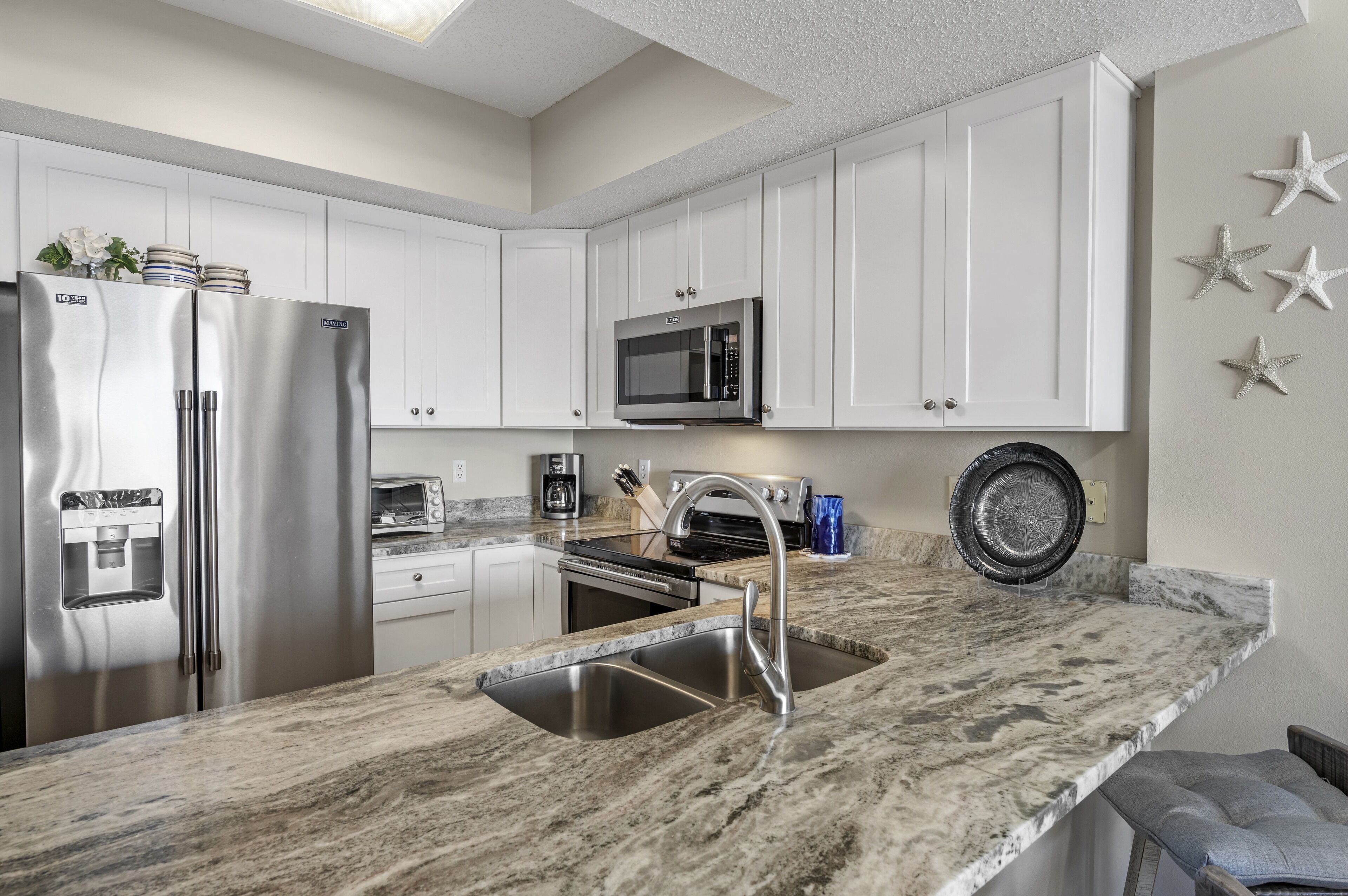 A modern kitchen with white cabinets, stainless steel appliances, a granite countertop, and a built-in microwave.