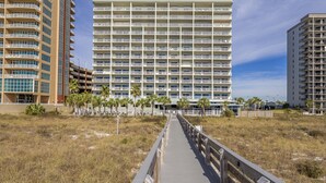 A multi-story hotel with a central atrium, surrounded by a boardwalk and palm trees. - Tidewater 307 | Perfect Location, Magnificent Views | Indoor/Outdoor Pools (Orange Beach)