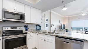 A modern kitchen with stainless steel appliances, white cabinetry, and a large window overlooking a balcony. - Tidewater 307 | Perfect Location, Magnificent Views | Indoor/Outdoor Pools (Orange Beach)