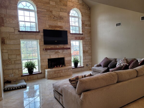 A living room with stone walls, a fireplace, a large flat-screen TV, and a beige sofa.