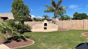 A well-maintained backyard with a stone fireplace, palm trees, and a clear blue sky. - Spacious family home with private pool in a safe, quiet neighborhood. (Glendale)