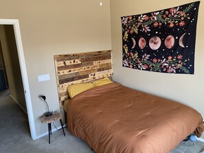 Een slaapkamer met een houten hoofdeinde, een bruine spreideken en een wandtapijt met maenen en bloemen.