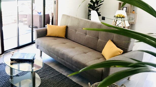 A living room with a grey sofa, a glass coffee table, a black rug, and a wicker basket.