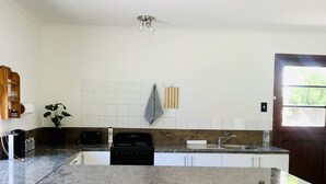 A modern kitchen with a large island, wooden stools, white cabinets, and a view of the outdoors through a door.