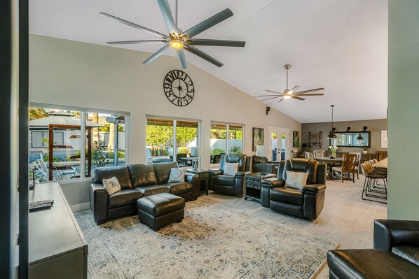 A spacious living room with leather sofas, a large rug, ceiling fans, and a clock on the wall.