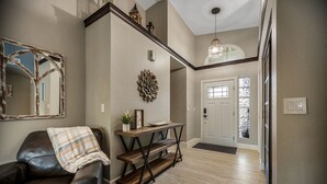 A hallway with a dark leather chair, a wooden console table, a decorative wall piece, and a door with windows. - Scottsdale Gem - Remodeled, Pool, Hot Tub (Scottsdale)
