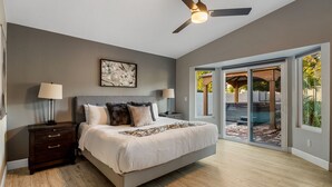 A bedroom with a bed, nightstands, a ceiling fan, and a large window with a view of the outdoors. - Scottsdale Gem - Remodeled, Pool, Hot Tub (Scottsdale)